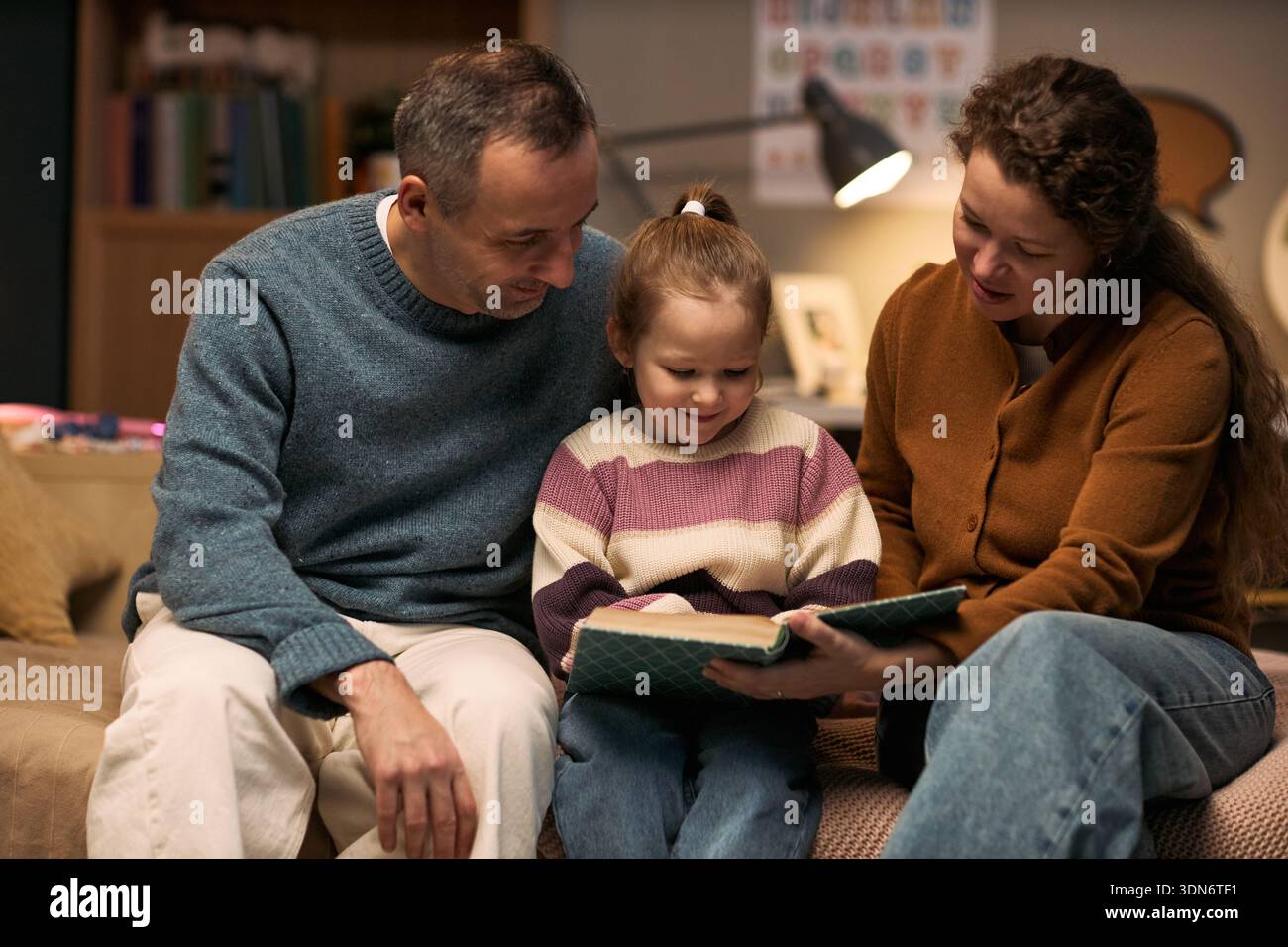 Homme d'âge moyen caucasien et femme d'âge moyen caucasien assis avec un enfant caucasien lisant le livre ensemble, enfant souriant pendant que les adultes engagent et soutiennent l'activité d'apprentissage Banque D'Images