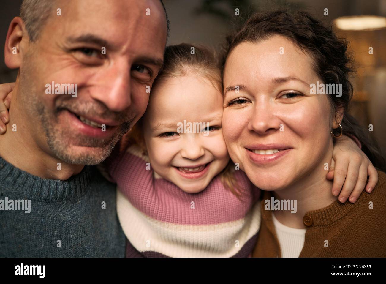 Portrait d'un homme caucasien d'âge moyen, d'une femme caucasienne et d'une fille caucasienne souriant étroitement ensemble, d'une fille enfantine embrassant des adultes, tous regardant dans la caméra Banque D'Images