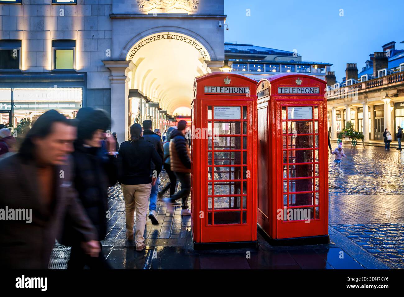 LONDRES, ROYAUME-UNI. 15 février 2025. Les gens marchent devant l'arcade Royal Opera House et les cabines téléphoniques rouges traditionnelles au crépuscule. Banque D'Images