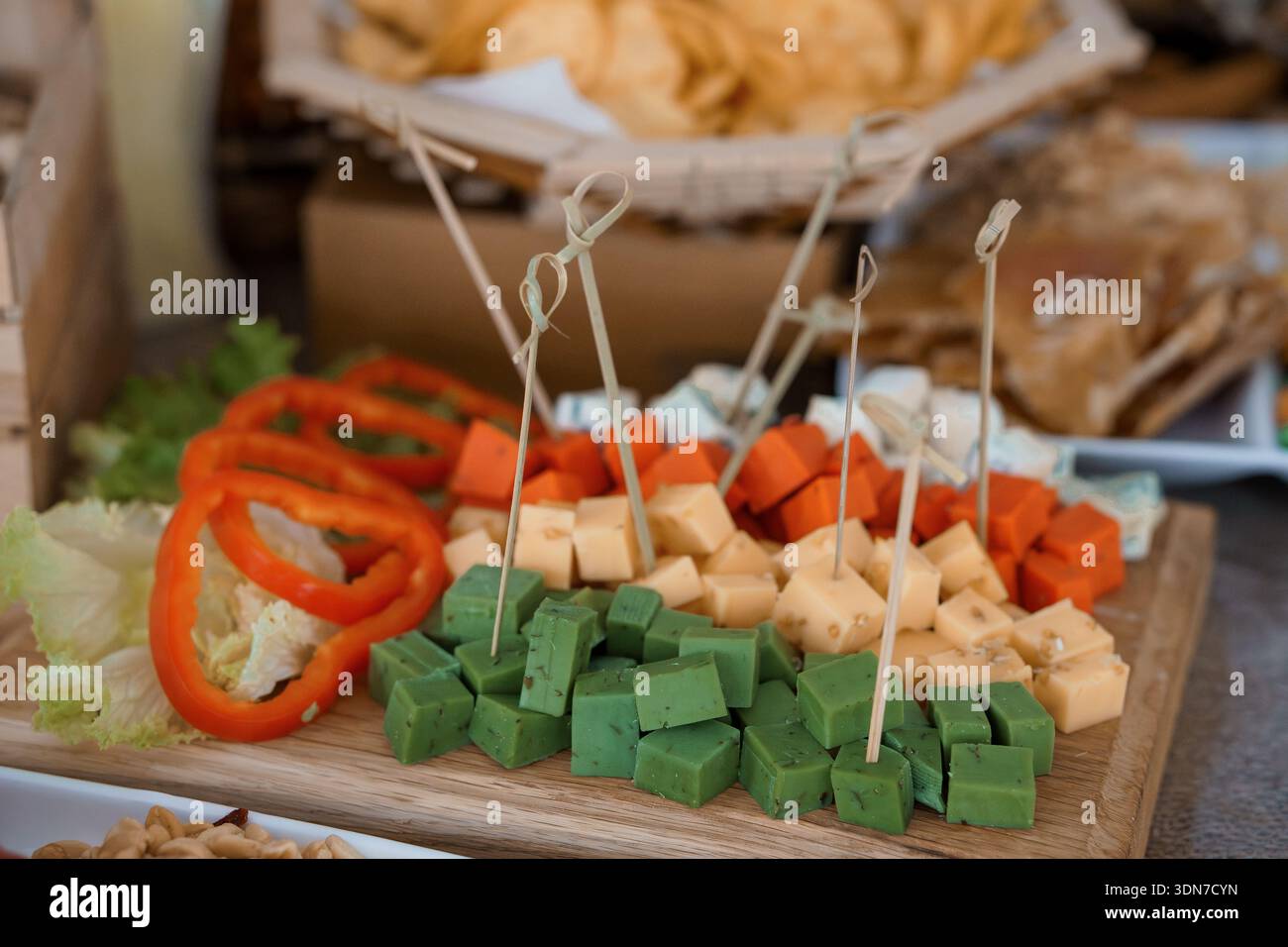 Un plateau de charcuterie éclatant propose un assortiment de fromages, des poivrons rouges frais, des cubes infusés d'herbes vertes et de la laitue croustillante, idéal pour les fêtes ou les repas Banque D'Images