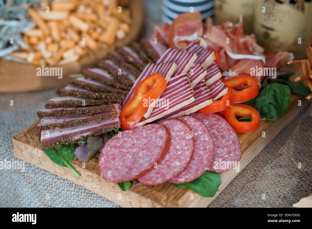 Une charcuterie magnifiquement arrangée avec charcuterie charcuterie, salami, prosciutto, poivrons rouges, épinards, et des gressins sur un plateau en bois rustique, Banque D'Images