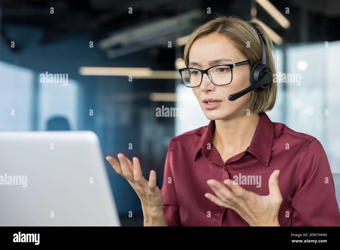 Représentant stressé du service client portant un casque, communiquant avec les clients et signalant de la confusion ou des problèmes lorsqu'il travaille sur un ordinateur portable dans un bureau moderne Banque D'Images
