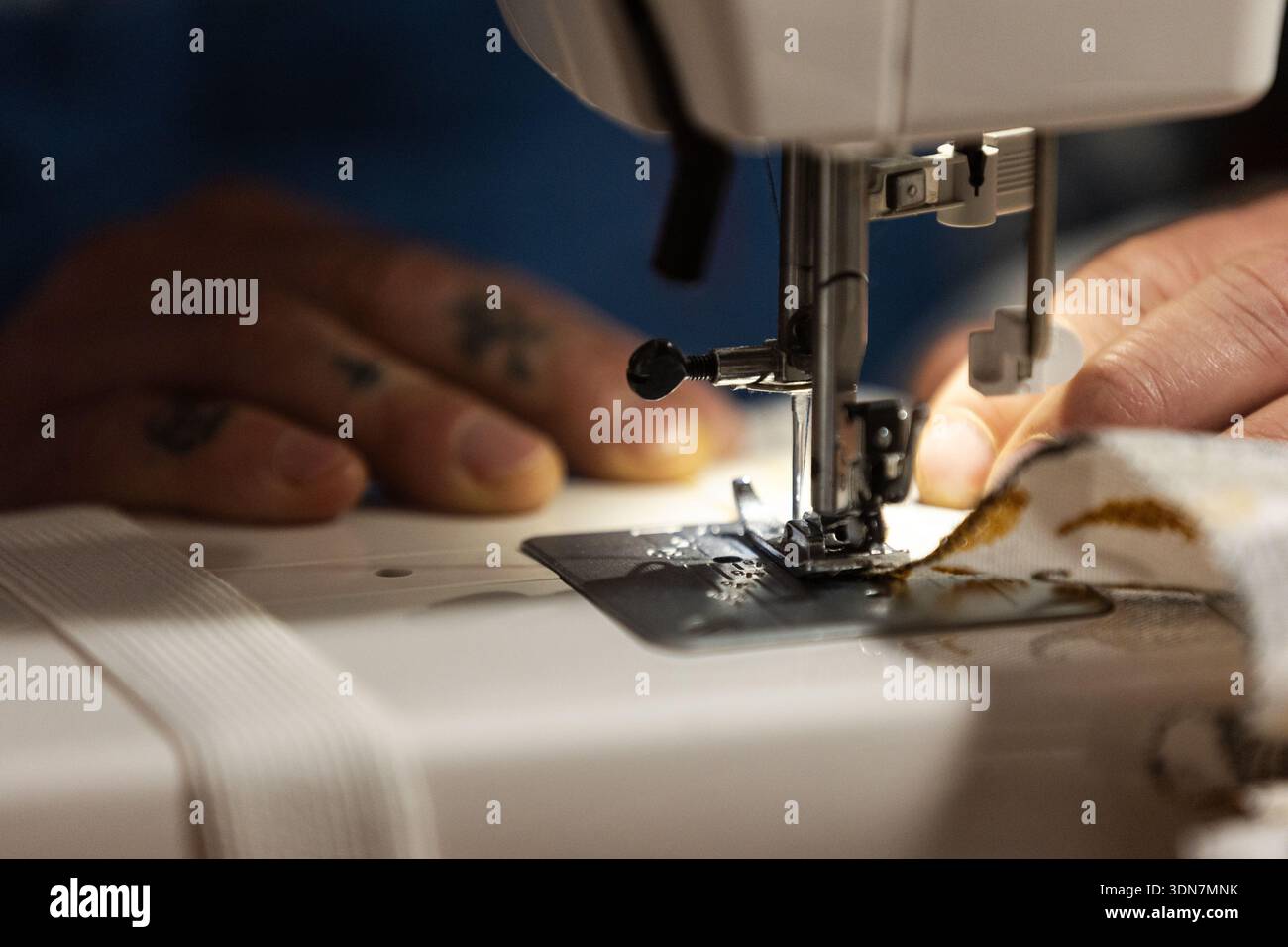 Mains actionnant une machine à coudre, créant un vêtement en tissu Banque D'Images