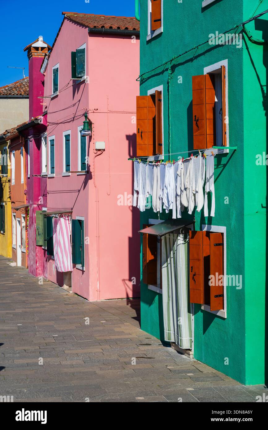 Bâtiments colorés avec des vêtements séchant sur une rue ensoleillée dans un quartier animé. Burano, lagune vénitienne, Italie Banque D'Images