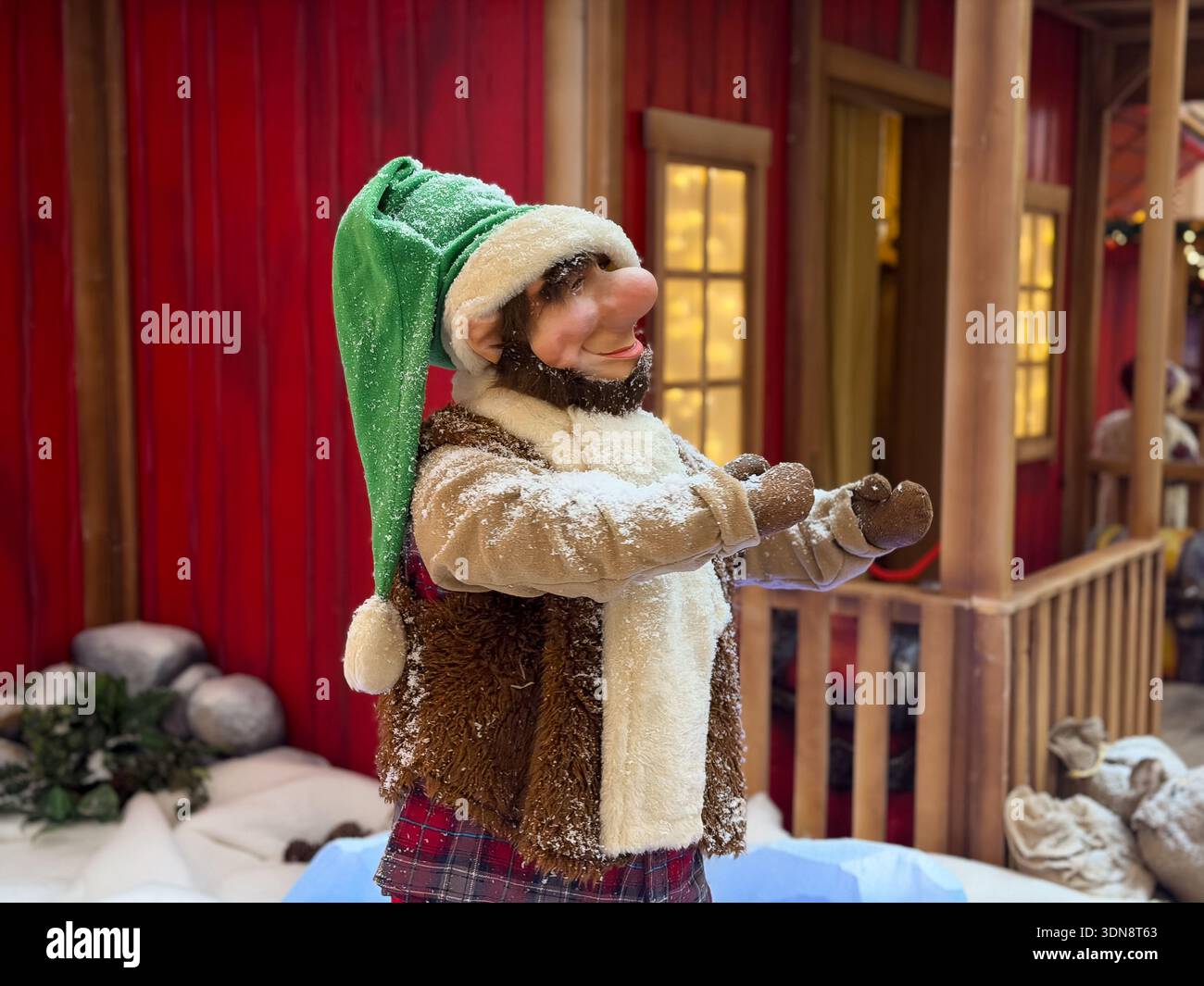 Gros plan d'une poupée décorative gnome de Noël, portant un grand chapeau vert, une écharpe blanche fourrée et un gilet brun, debout dans une confortable vacance enneigée Banque D'Images