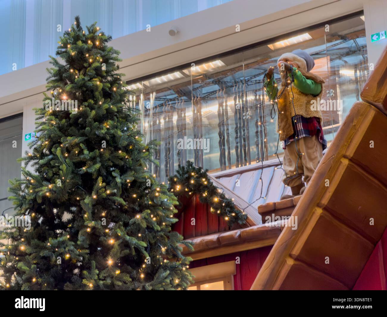 Un sapin de Noël magnifiquement illuminé et une figurine de poupée fantaisiste tenant des ficelles illuminent l'atmosphère festive d'un centre commercial moderne Banque D'Images