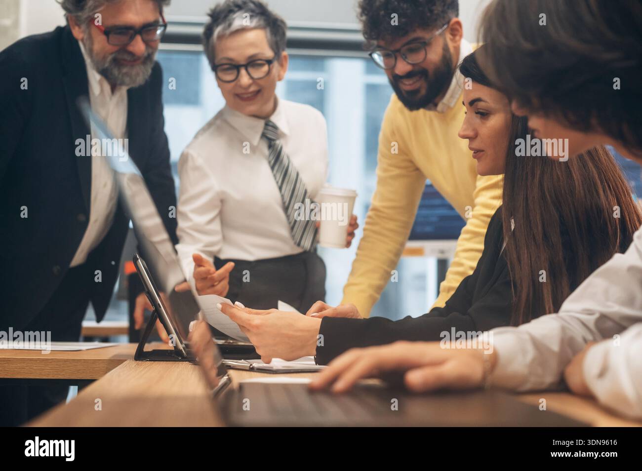 Divers membres de l'équipe se sont engagés dans une discussion collaborative autour d'un ordinateur portable dans un bureau contemporain, partageant des idées et des stratégies pour un pro efficace Banque D'Images