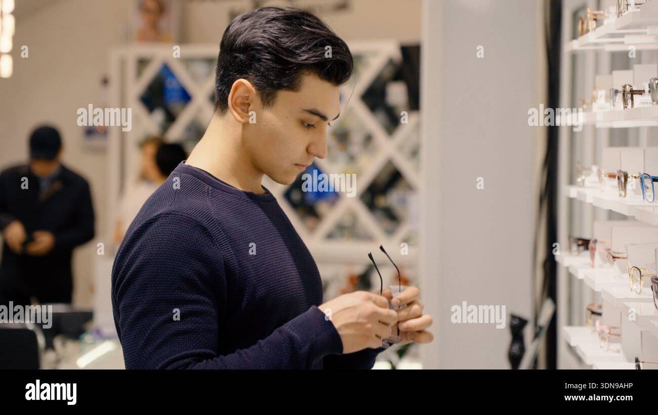 Jeune homme nettoyant des lunettes avec un chiffon en microfibre dans la boutique Banque D'Images