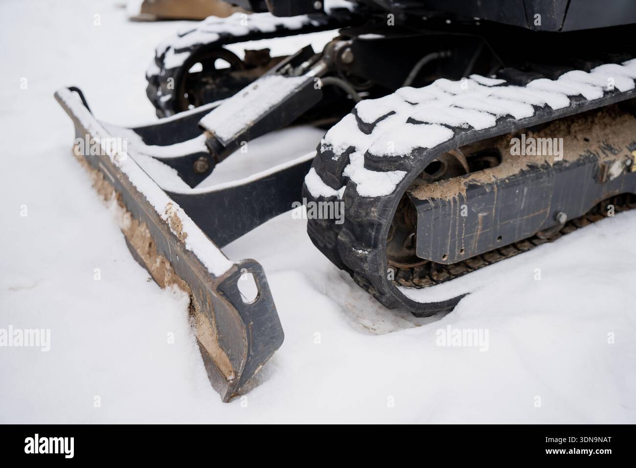 Chaîne en caoutchouc compacte pour chargeuse à chaînes avec bande de roulement enneigée et train de roulement boueux à côté de la lame de bouteur avant, photographiée en hiver Banque D'Images
