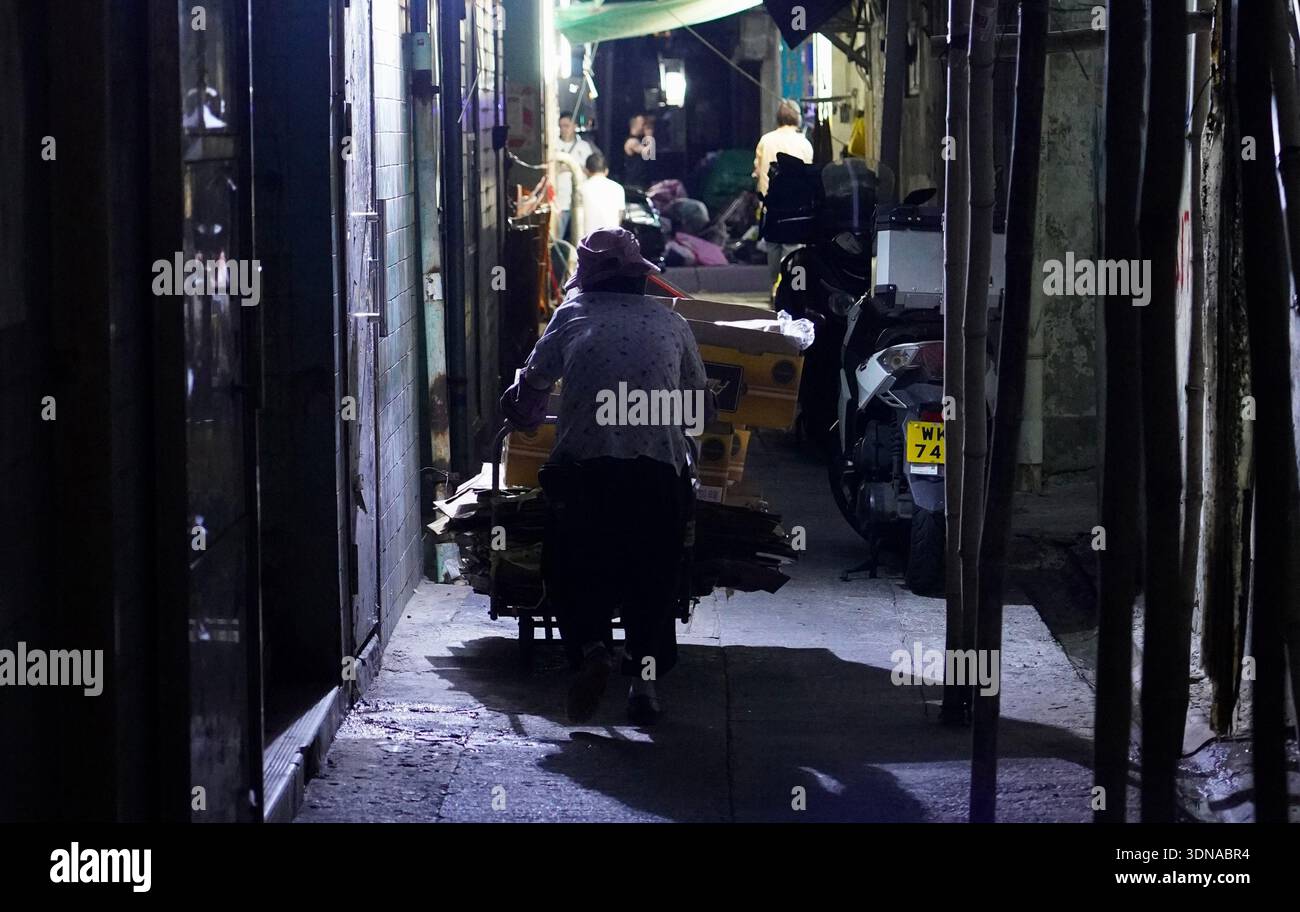 Une vieille dame travaille tard dans la nuit pour faire un peu plus d'argent en collectant des boîtes en carton des entreprises voisines. Banque D'Images