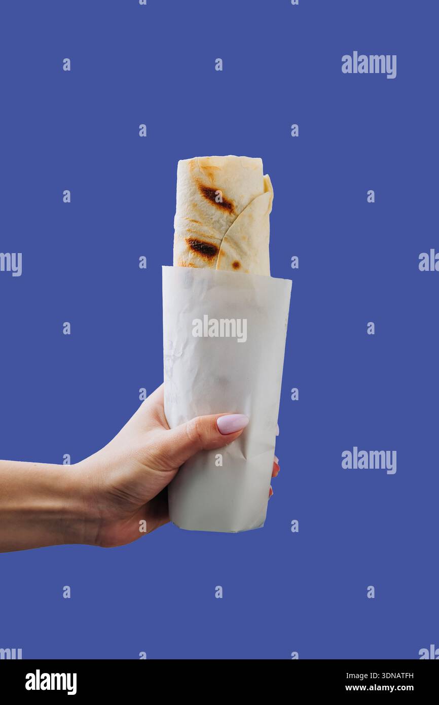 Main tenant shawarma enveloppé dans une pochette en papier isolé sur fond bleu Banque D'Images