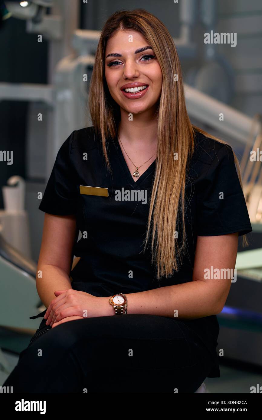 Professionnel de santé féminin souriant dans les gommages noirs assis dans le cadre de clinique moderne pour photo stock Banque D'Images