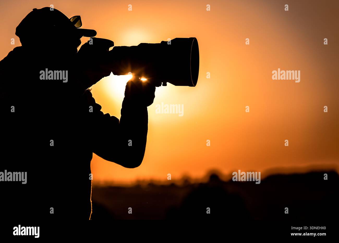Une personne capture un coucher de soleil avec une caméra en extérieur. Le soleil crée une lueur brillante derrière. Banque D'Images