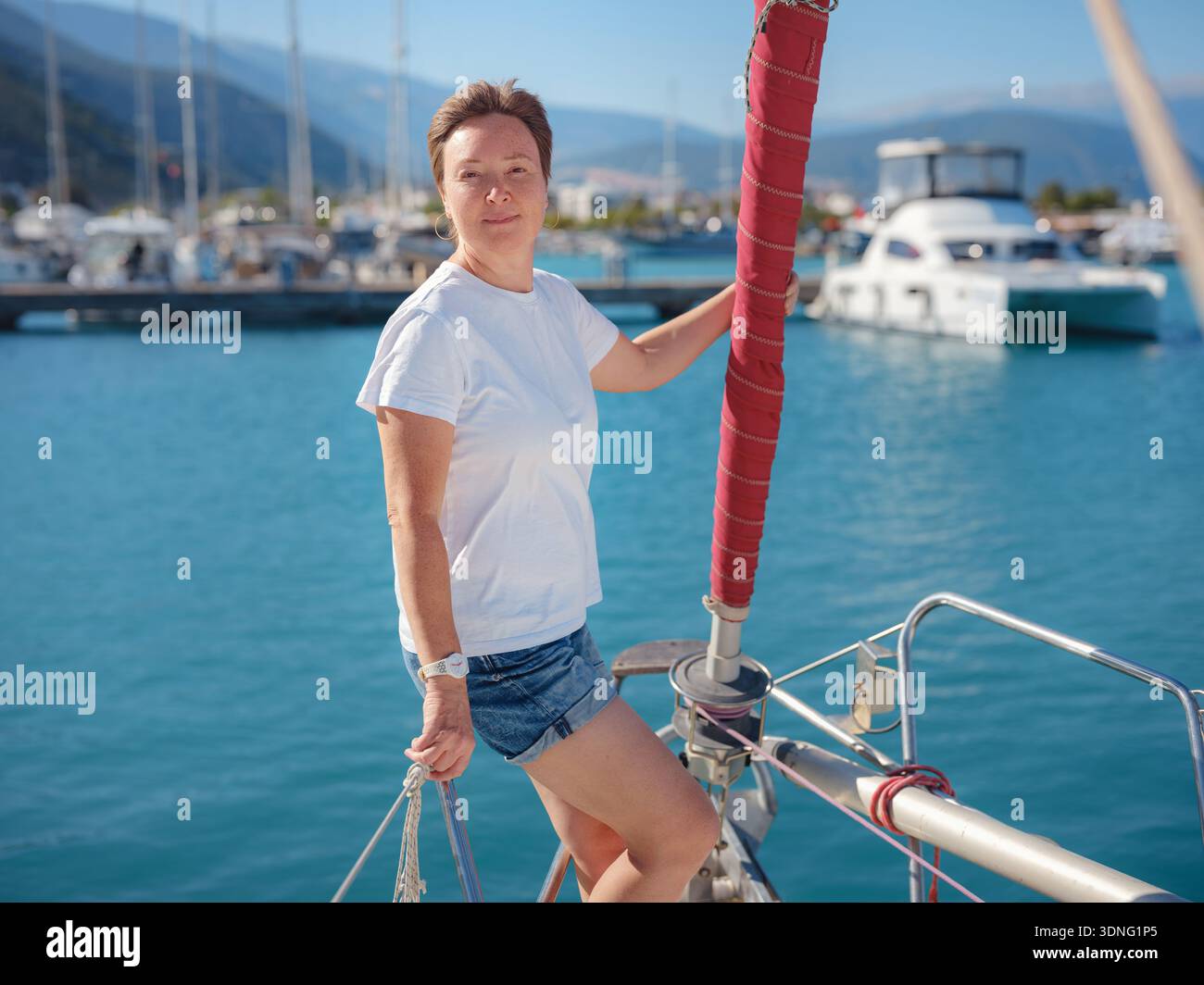 Femme marin tient le tissu de voile blanc se préparant à lever des voiles sur le yacht. L'activité physique et les compétences de maniement de bateau sont montrées pendant la préparation pour le voyage en voilier près de la côte de Finike. Banque D'Images