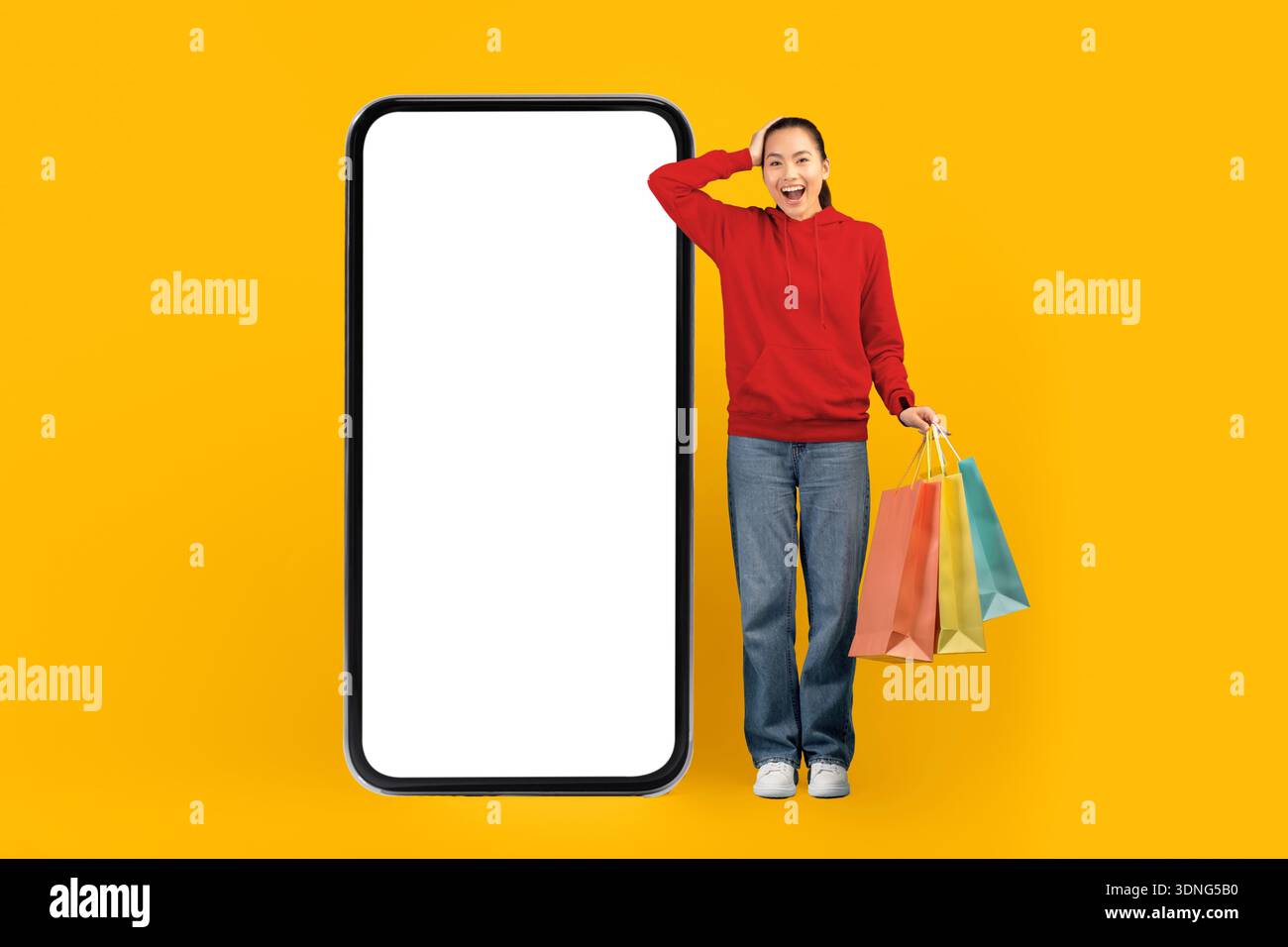 Personne souriante se tient avec des sacs à provisions à côté d'un grand smartphone sur un fond jaune vif Banque D'Images