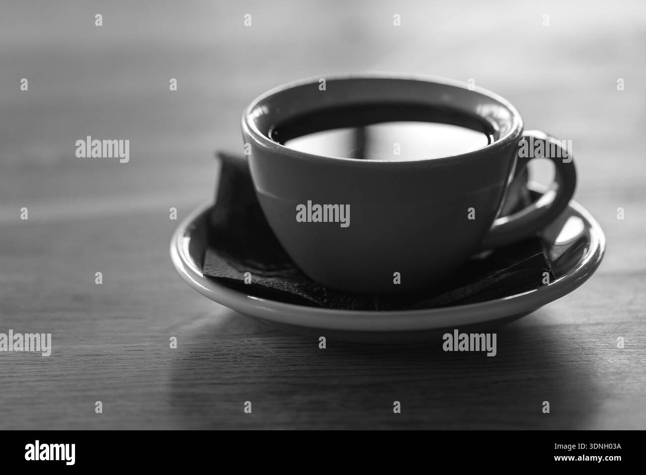 Une image monochrome d'une tasse de café simple sur une soucoupe, posée sur une table en bois. Évoque les rituels matinaux, les moments calmes et les vibrations douillettes de café sans distra Banque D'Images