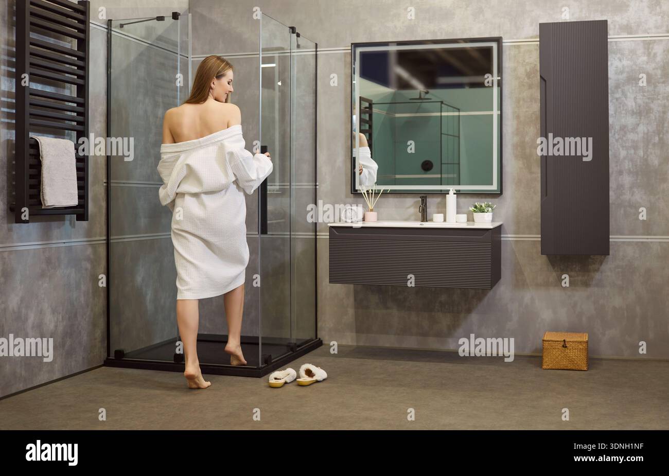Vue arrière d'une femme portant un peignoir blanc, allant avoir une douche dans la cabine de douche Banque D'Images