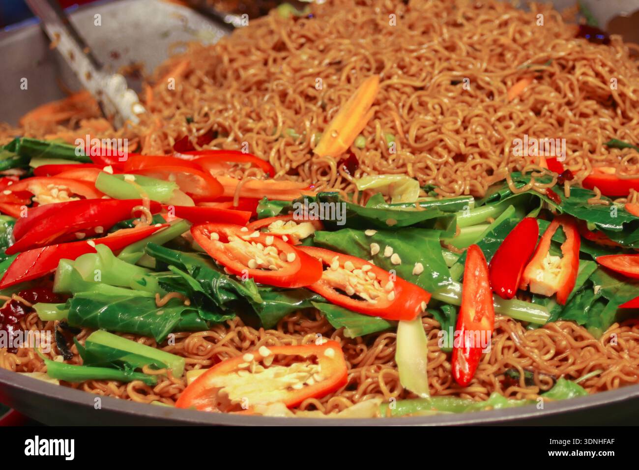 Nouilles sautées thaïlandaises épicées avec Chili rouge et légumes verts dans le cadre du marché nocturne. Image authentique de cuisine de rue. Banque D'Images