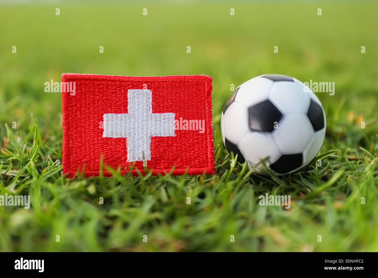 Drapeau suisse et ballon de football sur l'herbe du stade. Symbolique de la fierté sportive nationale et journée de match de compétition internationale de football. Banque D'Images
