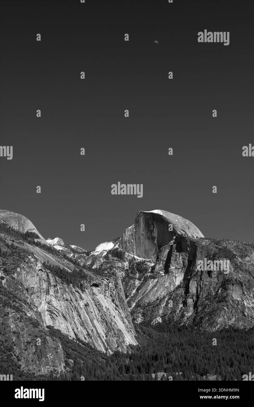 Une demi-lune pend parfaitement au-dessus de la face granitique pure du Half Dome dans le parc national de Yosemite, en Californie. Le monolithe emblématique s'élève de façon spectaculaire ag Banque D'Images