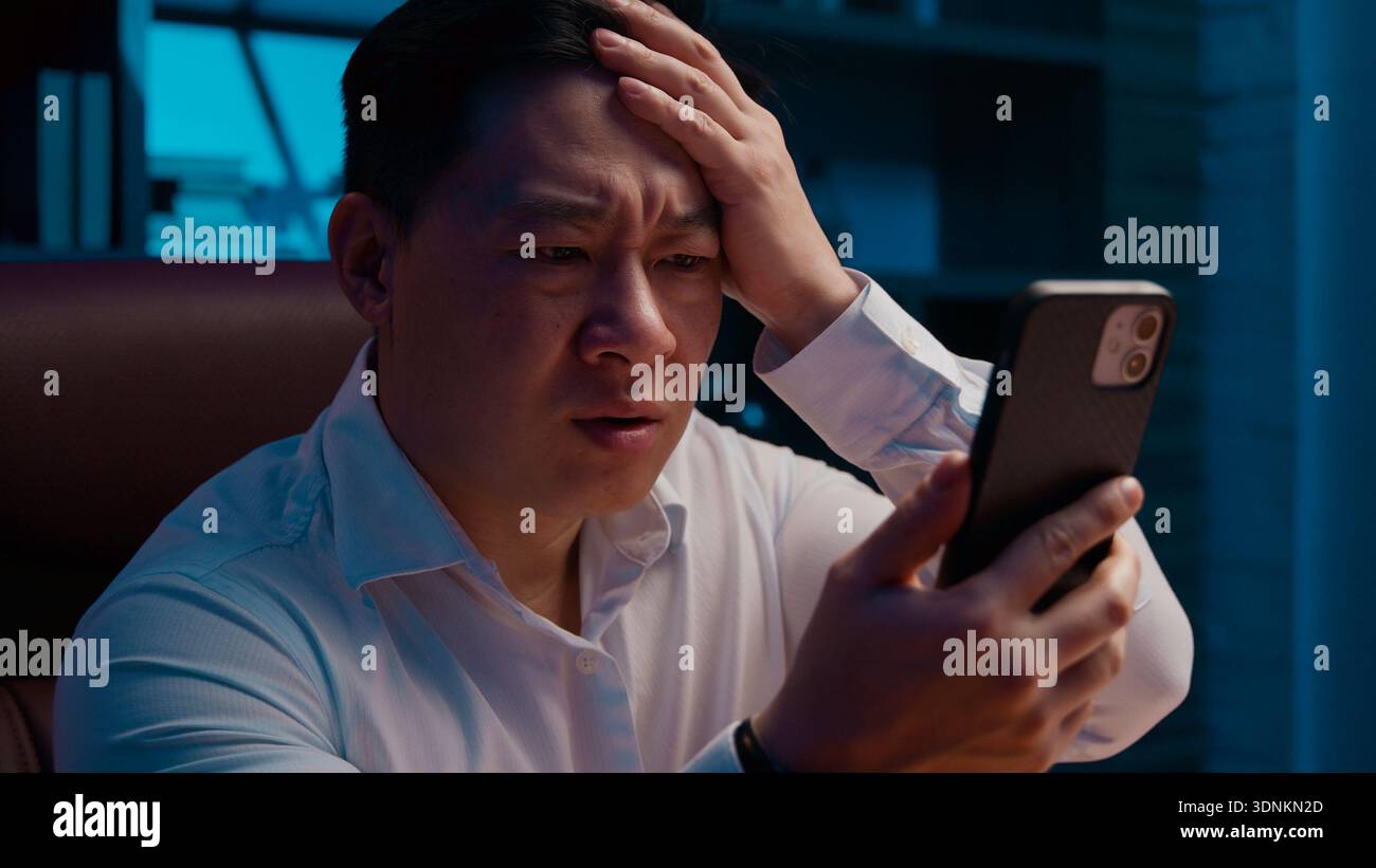 Bouleversé souligné l'échec asiatique d'homme d'affaires d'âge moyen avec téléphone mobile la nuit bureau soir triste frustré homme d'affaires coréen avec smartphone échouer Banque D'Images