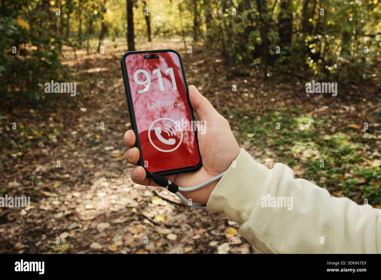 Main tenant un smartphone montrant un écran d'appel d'urgence 911 dans un chemin forestier. Concept de danger, demande d'aide urgente, risque d'accident extérieur et Banque D'Images