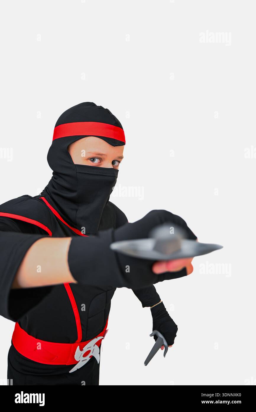 Enfant habillé comme un shuriken ninja visant dans la pose d'action avec un look concentré. Banque D'Images