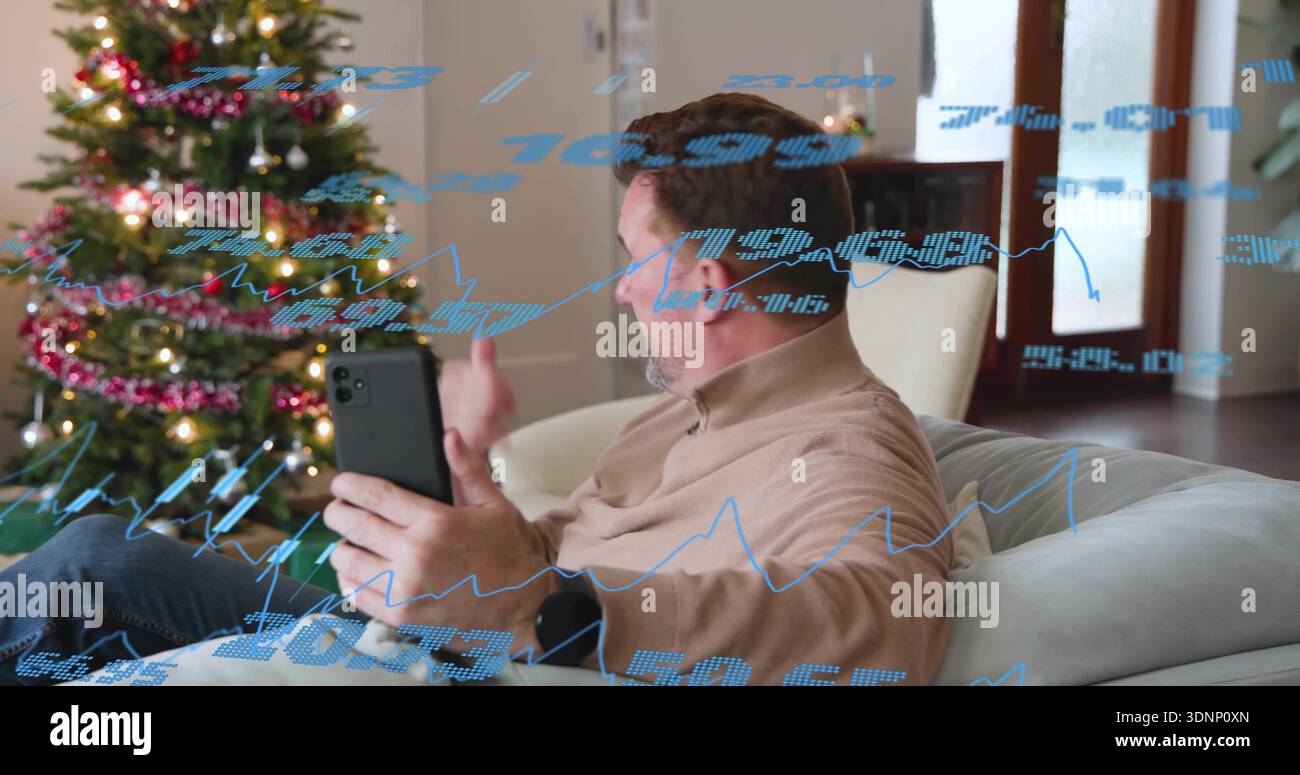 Tenant smartphone, homme en chemise beige geste sur canapé avec arbre de Noël et cartes bleues superposées Banque D'Images