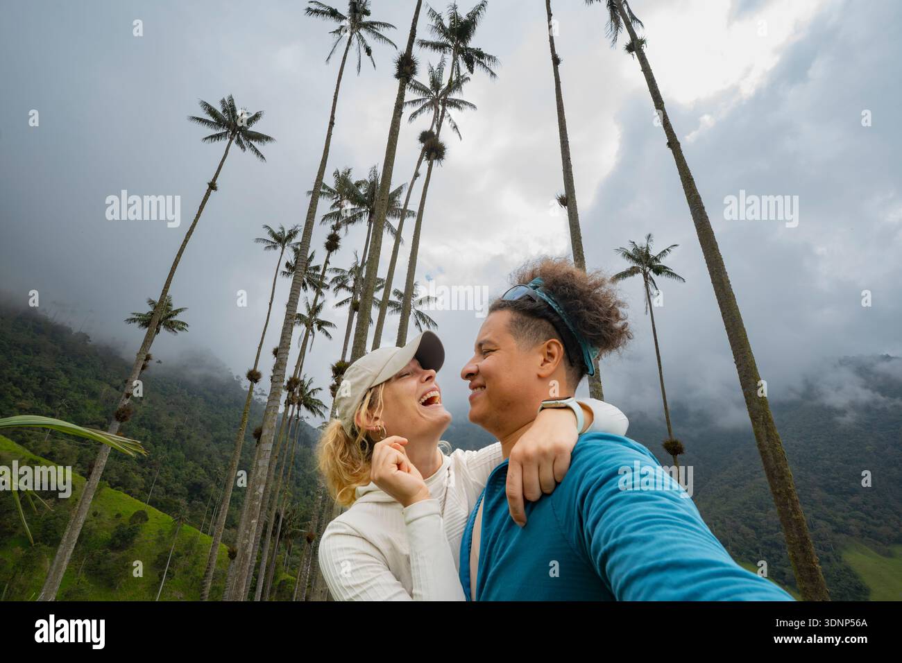 Un couple joyeux s'embrasse sous les imposants palmiers de cire de la luxuriante vallée de Cocora en Colombie. Les nuages brumeux et la verdure vibrante créent une superbe BA naturelle Banque D'Images