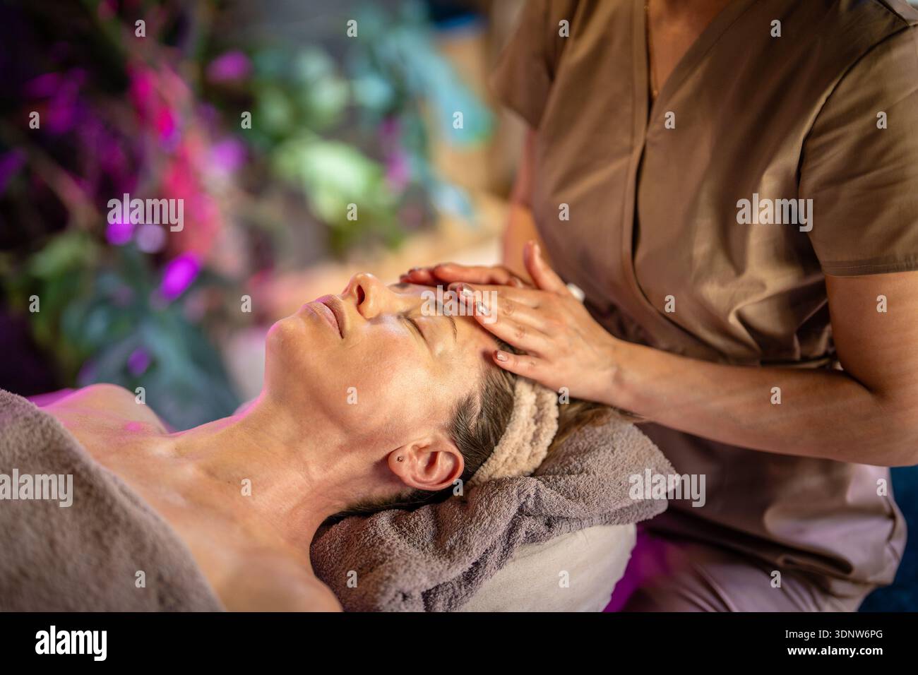 Femme rêveuse recevant un traitement de massage facial relaxant de guérison avec des huiles aromatiques en clinique de beauté Banque D'Images