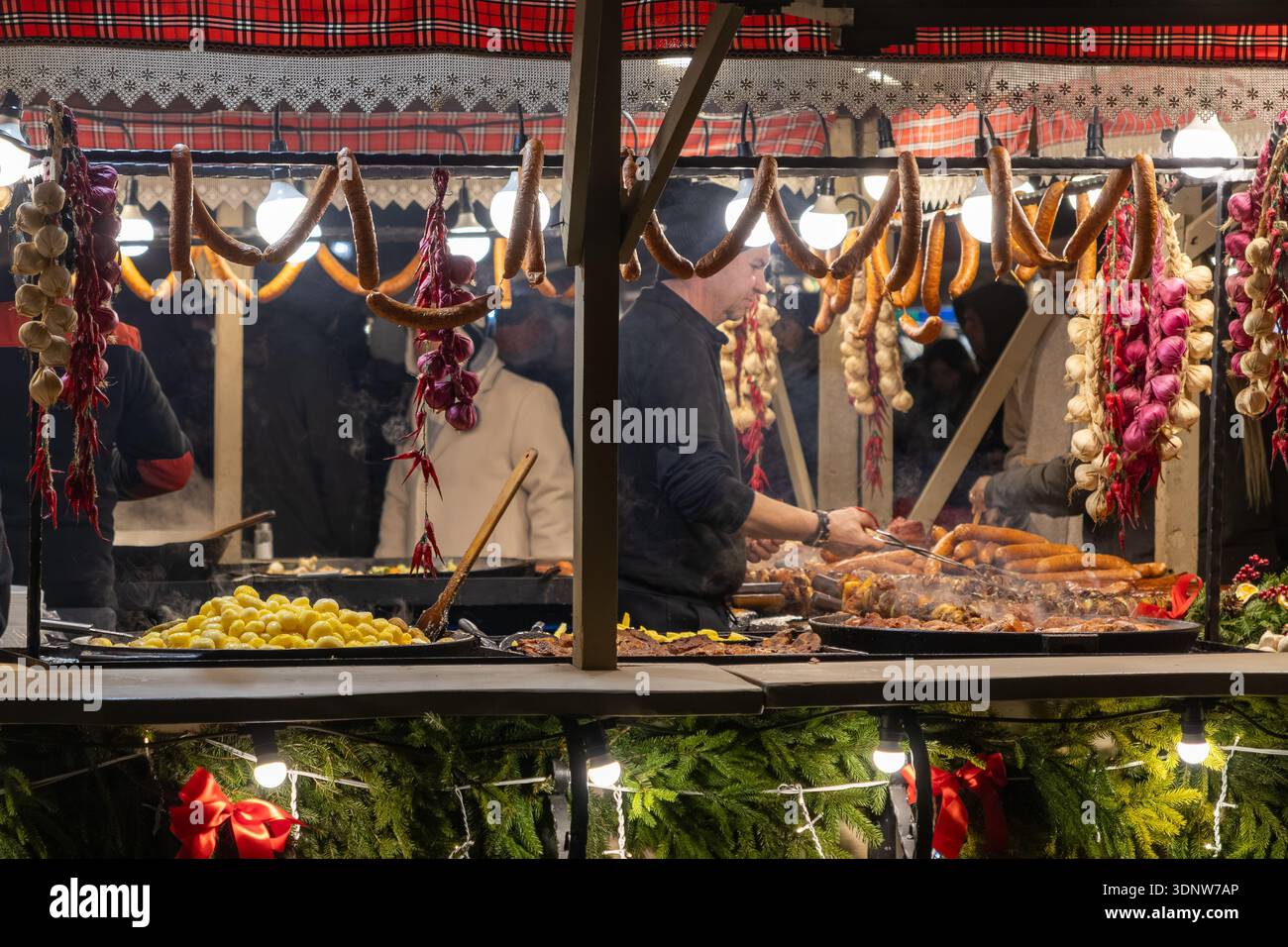 Cracovie, Pologne - 30 novembre 2025 : marché animé avec un vendeur cuisinant des saucisses grillées et des pommes de terre, mettant en valeur le culi festif de l'hiver Banque D'Images