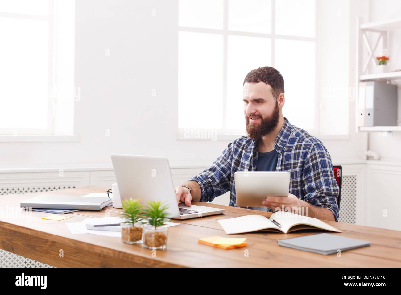 Jeune homme souriant à l'aide d'un ordinateur portable dans un bureau blanc moderne Banque D'Images