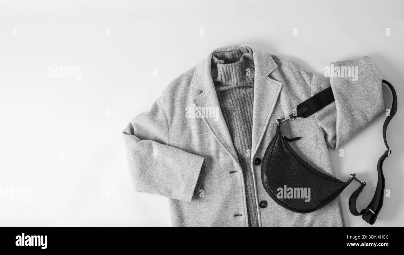 Style monochrome. Manteau ou veste en laine gris clair, pull en cachemire gris foncé et sac en cuir noir isolé sur fond de tissu neutre. Automne Banque D'Images