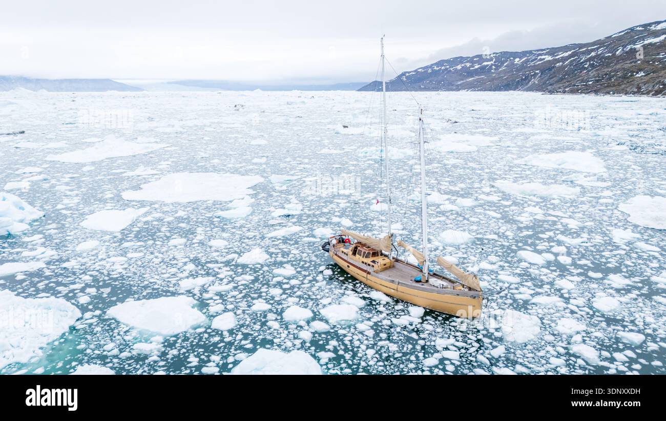 Un voilier solitaire navigue dans les eaux glacées du détroit de Davis, au Groenland, entouré d'icebergs flottants. La scène tranquille capture la beauté brutale Banque D'Images