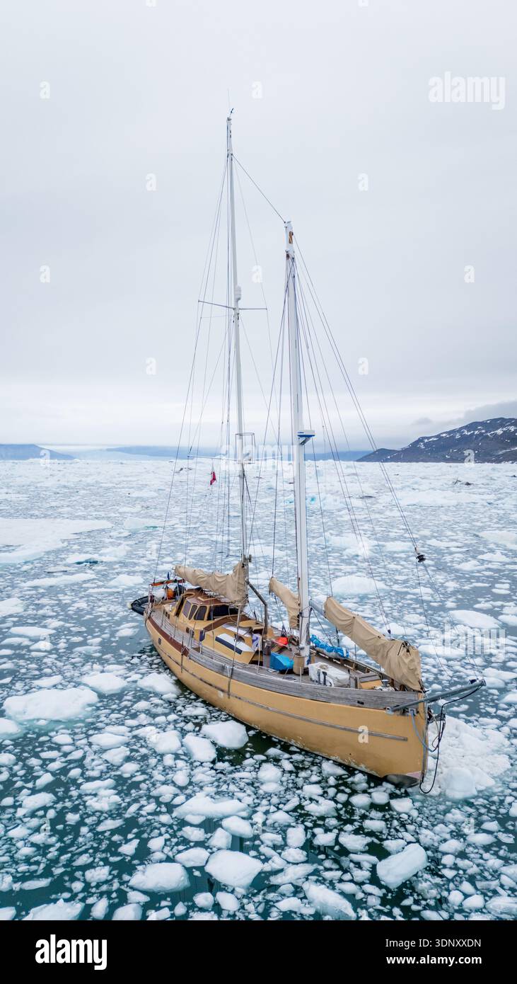 Un voilier navigue gracieusement à travers les eaux glacées du détroit de Davis, au Groenland, entouré d'icebergs flottants et de vastes paysages marins sous un CLO Banque D'Images