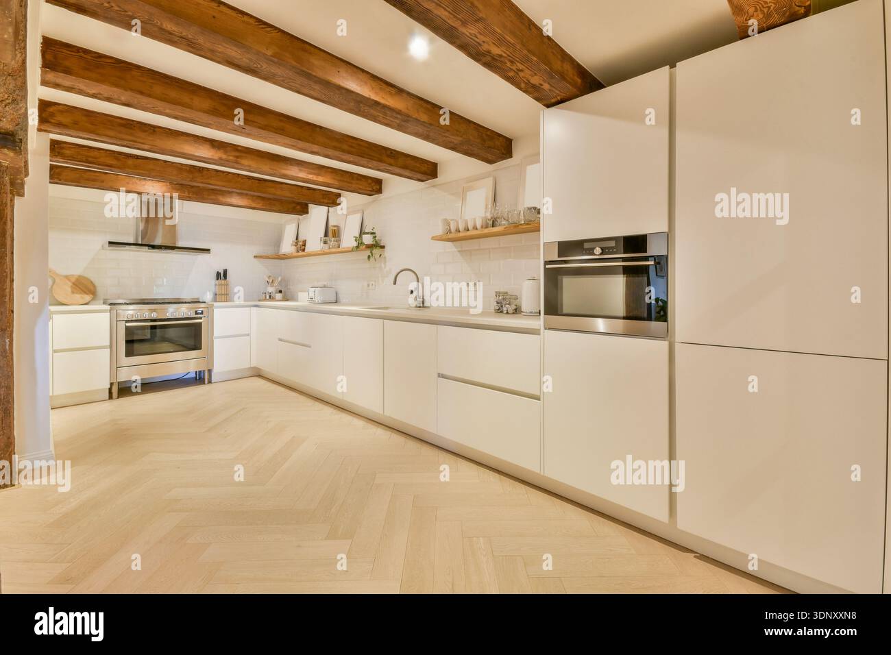Cuisine moderne lumineuse et spacieuse avec armoires blanches élégantes, appareils électroménagers en acier inoxydable et poutres en bois. Le design minimaliste est accentué Banque D'Images