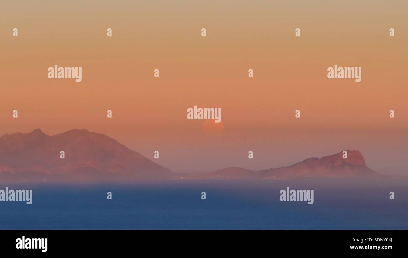 Vue aérienne des montagnes entourées d'une brume douce et chaude, avec le soleil apparaissant comme un orbe ardent à l'horizon, Cape Town, Western Cape, Afrique du Sud. Banque D'Images