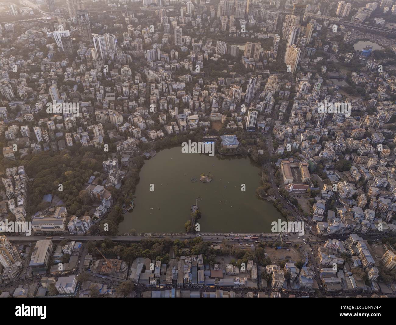 Vue aérienne d'une ville animée entourant un lac serein aux teintes vertes, contrastant avec des bâtiments et des routes denses, capturés dans la douce lumière dorée Banque D'Images