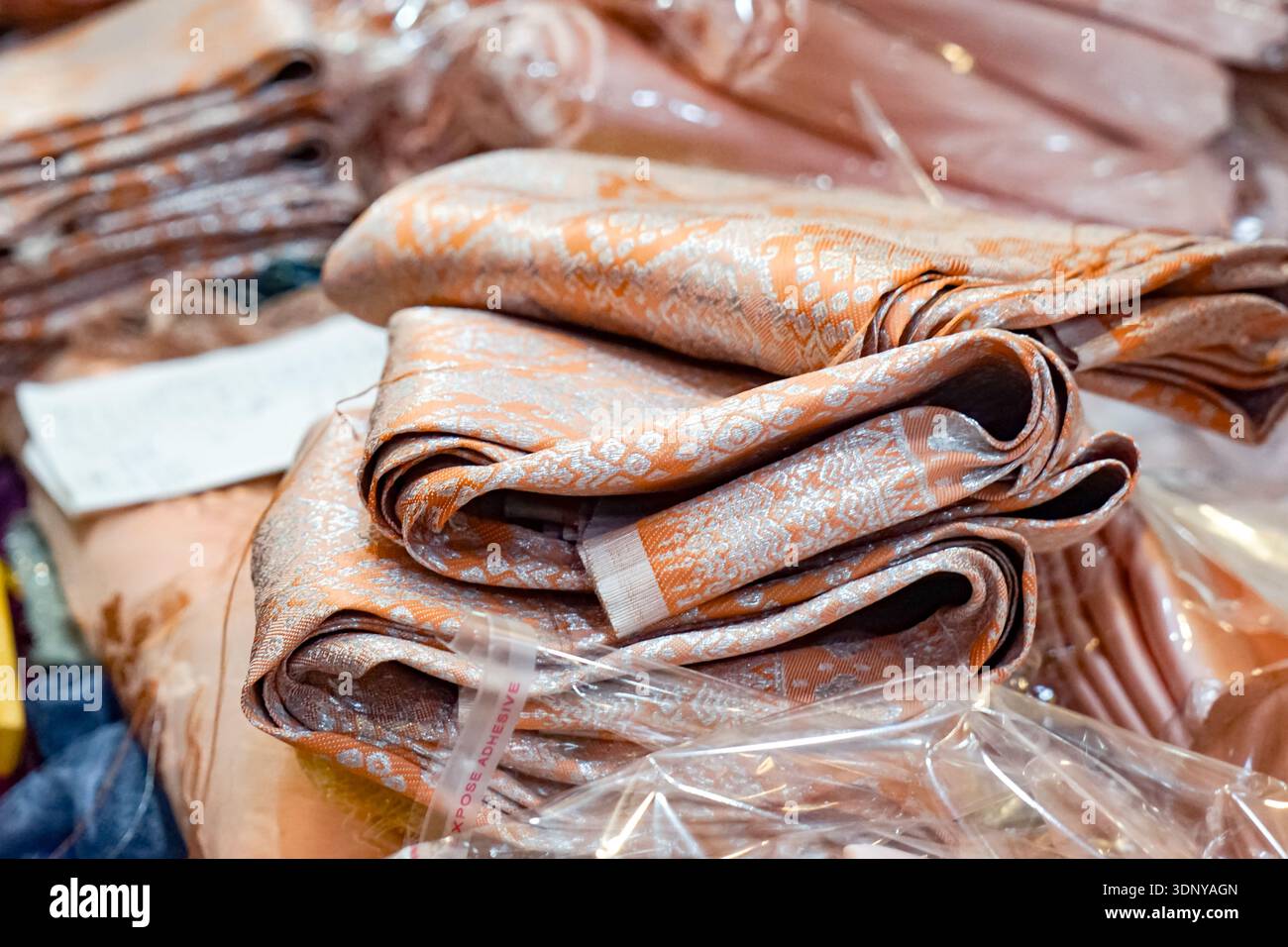 Gros plan d'un tissu décoratif ressemblant à de la soie avec des motifs tissés oranges et argentés détaillés. Banque D'Images