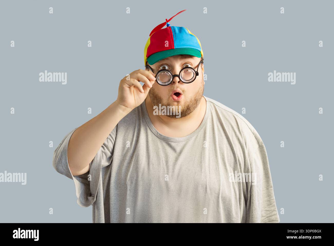 Homme en surpoids surpris dans un chapeau d'hélice coloré et des verres ronds, comique Banque D'Images