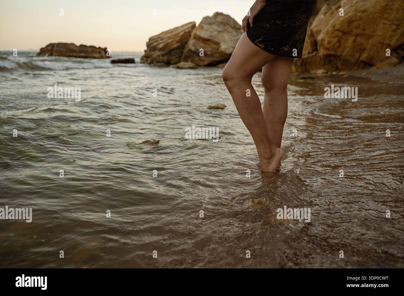 Silhouette sombre d'une femme debout dans la mer sur un fond rocheux. Concept de force, de beauté naturelle et d'humeur contemplative lors d'un Seasid Banque D'Images