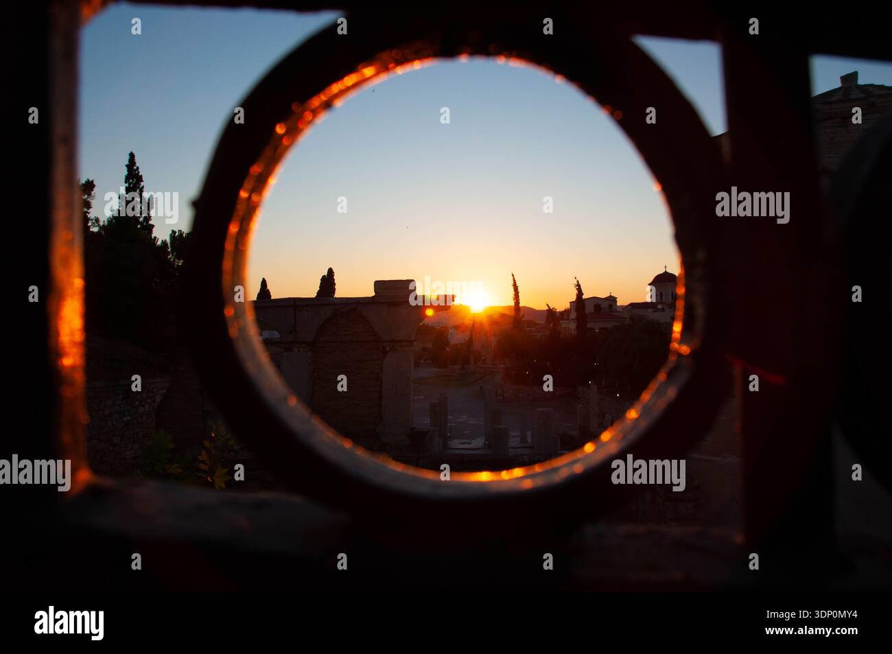 Paysage pittoresque de coucher de soleil italien vu à travers un cadre de clôture circulaire, capturant des silhouettes d'arbres et de bâtiments dans un ciel vibrant. Banque D'Images
