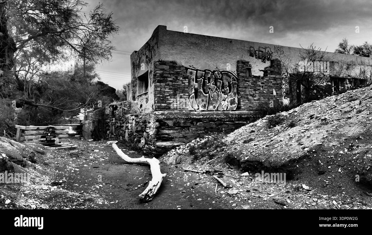 Photographie en noir et blanc d'une structure côtière abandonnée en Grèce avec des murs de pierre recouverts de graffitis, des ouvertures brisées et des débris dispersés dans le Banque D'Images