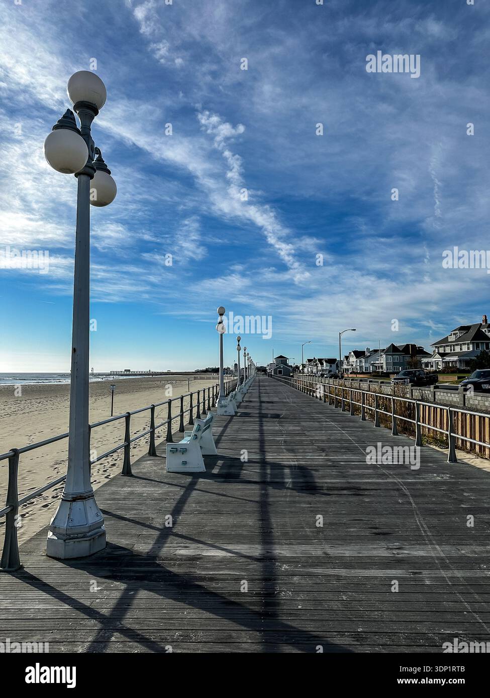 Promenade en bois s'étendant le long d'une plage de sable sous un ciel bleu avec des nuages éparpillés. La promenade est flanquée de lampadaires de style vintage Banque D'Images