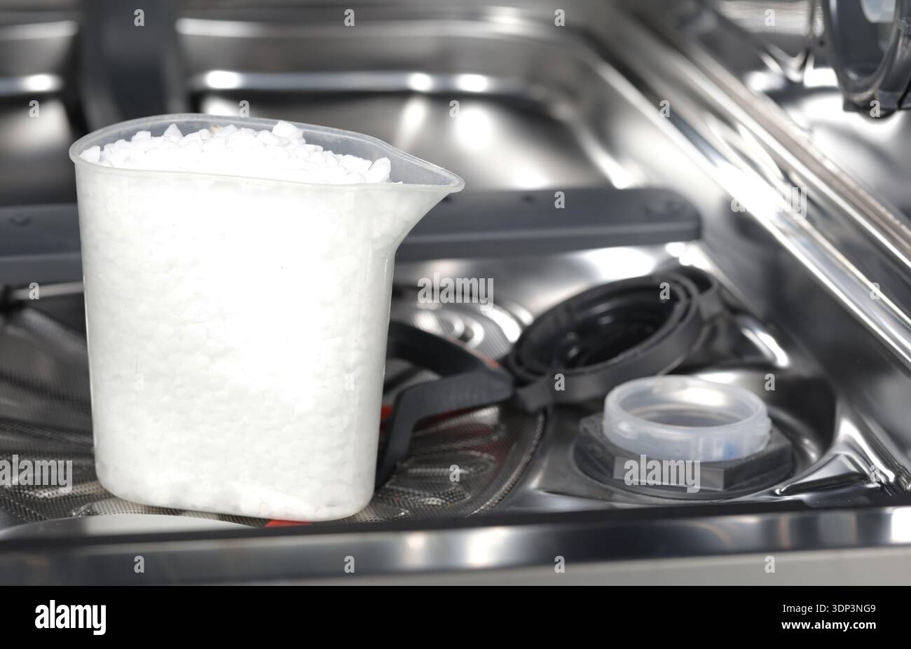 Sel granulaire blanc pour lave-vaisselle dans une tasse graduée transparente. Tasse à l'intérieur d'un lave-vaisselle moderne. Ouvrez le réservoir de sel pour le système d'adoucissement de l'eau, vital pour le nettoyage Banque D'Images