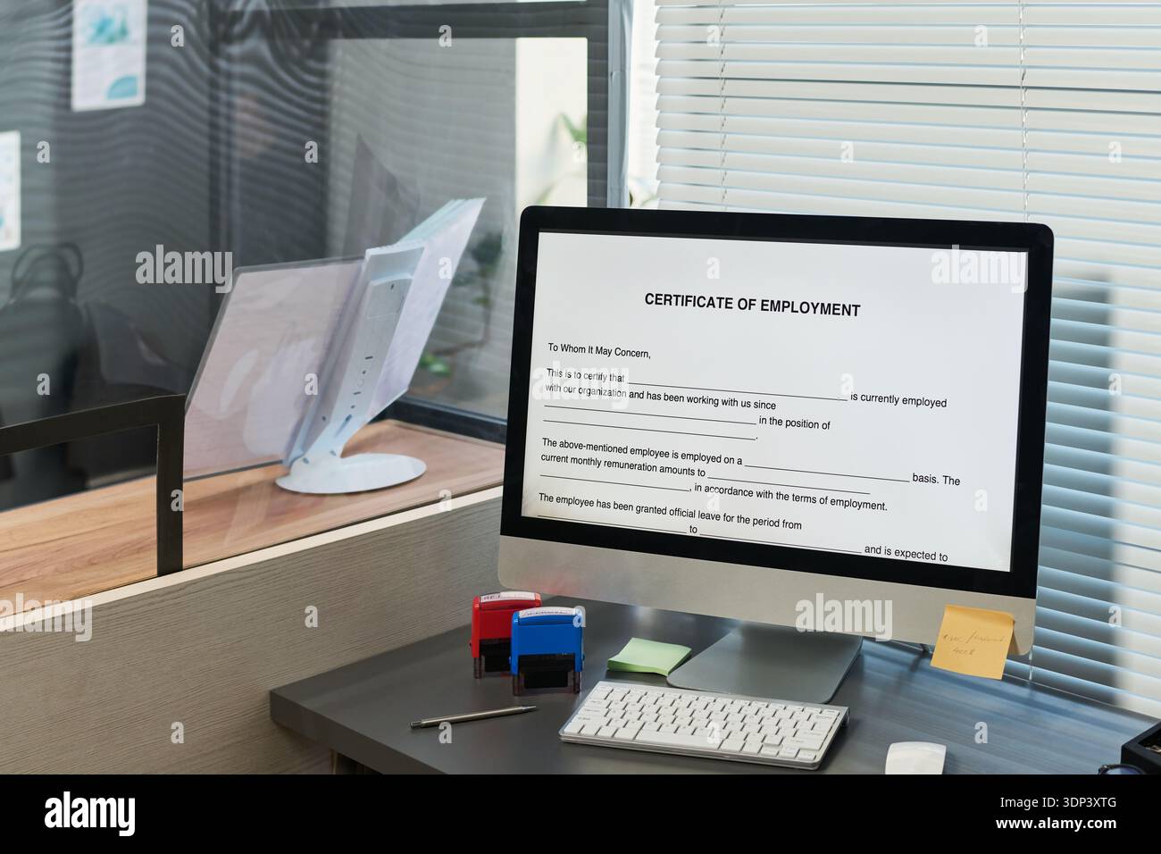 Moniteur d'ordinateur de bureau affichant le certificat de document d'emploi sur l'écran, espace de travail de bureau avec stores et cloison de verre, contexte de centre de visa suggérant le processus de vérification de document Banque D'Images