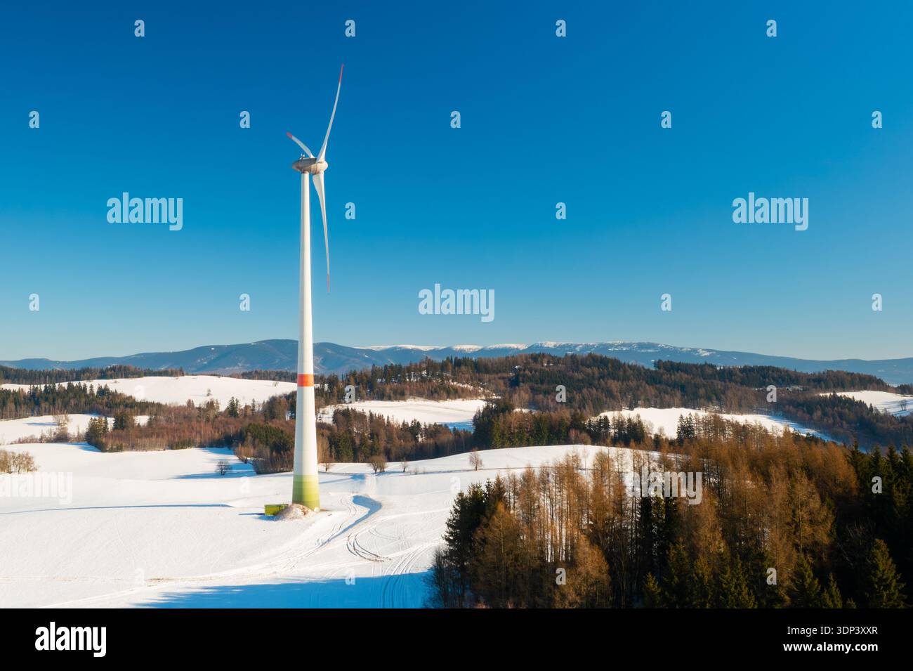 Une éolienne fonctionne dans un champ ouvert recouvert de neige pendant l’hiver, symbolisant l’adaptation au climat grâce à des solutions d’énergies renouvelables. Banque D'Images