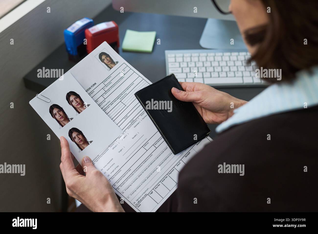 Femme caucasienne d'âge moyen détenant un passeport et un formulaire de demande de visa avec des photos d'identité jointes, assise au bureau dans le centre de visas, préparant des documents pour le traitement ou la vérification Banque D'Images
