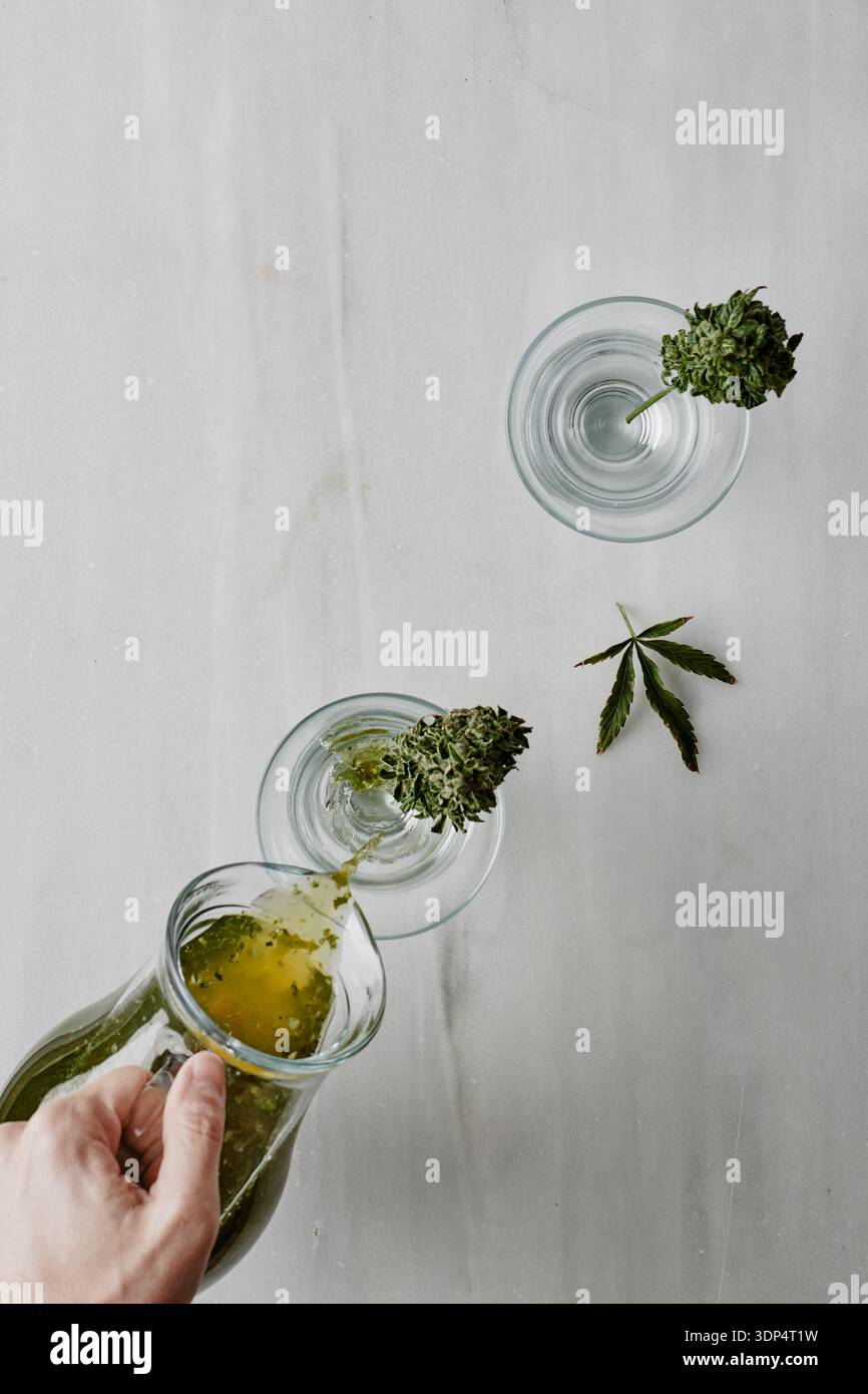 Verser le cocktail infusé de cannabis vert dans des verres sur une table en marbre Banque D'Images