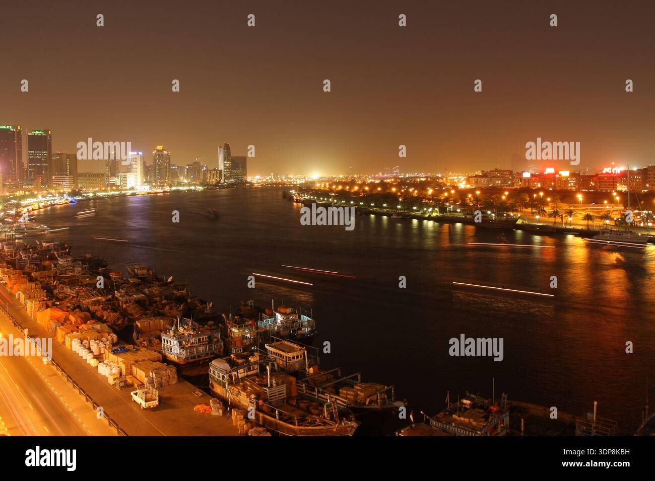 Vue nocturne du Dubai Creek avec gratte-ciel illuminés et traînées de lumière des embarcations qui passent Banque D'Images